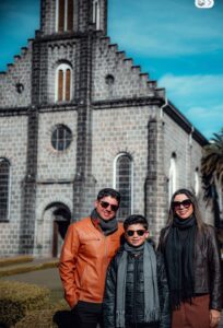 Família com dois adultos e uma criança em frente à Igreja São Pedro, um dos principais pontos turísticos de Gramado, durante viagem em família.