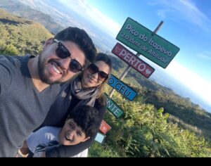 Família com dois adultos e uma criança em frente ao letreiro do Pico do Itapeva em Campos do Jordão