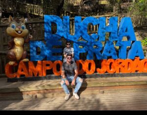 Adulto e criança em frente ao letreiro da Ducha de Prata em Campos do Jordão durante passeio em família
