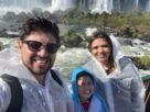 Pai, mãe e filho molhados observando as Cataratas do Iguaçu durante viagem em família a Foz do Iguaçu