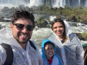 Pai, mãe e filho molhados observando as Cataratas do Iguaçu durante viagem em família a Foz do Iguaçu