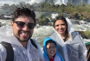 Pai, mãe e filho molhados observando as Cataratas do Iguaçu durante viagem em família a Foz do Iguaçu