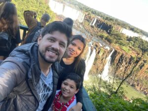 Glaziele, Rafael e Lucas na trilha das Cataratas do Iguaçu com uma das cachoeiras ao fundo durante passeio em família.
