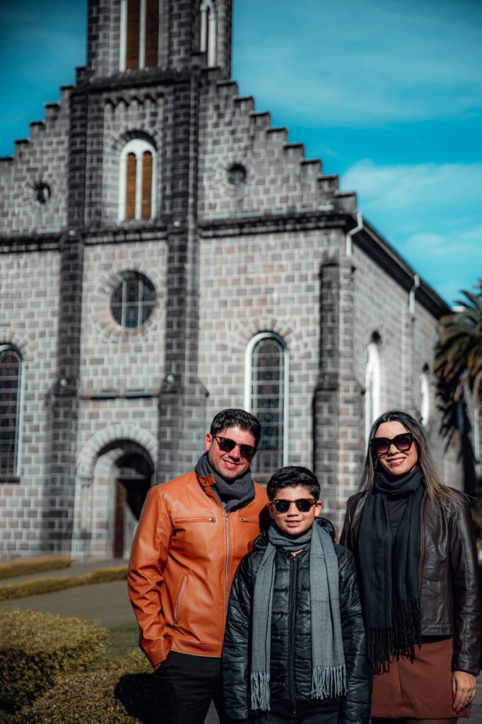Viagem em família em Gramado: casal com filho em frente à Igreja São Pedro.