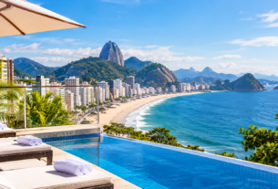 Vista panorâmica do Rio de Janeiro com praia, hotéis, montanhas e itens de viagem infantil em uma varanda