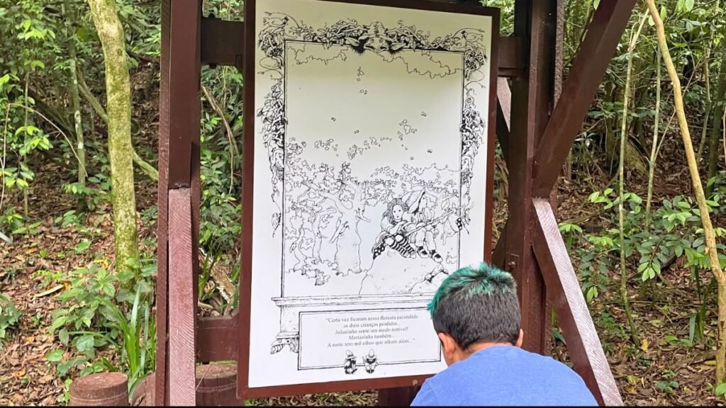 Curitiba com criança autista: Lucas observa uma ilustração da história de João e Maria na trilha do Bosque Alemão.