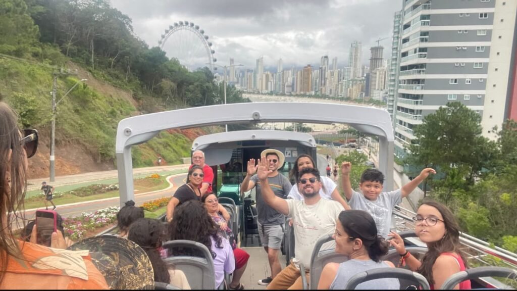 Família e outros passageiros em um ônibus turístico aberto durante passeio por Balneário Camboriú.