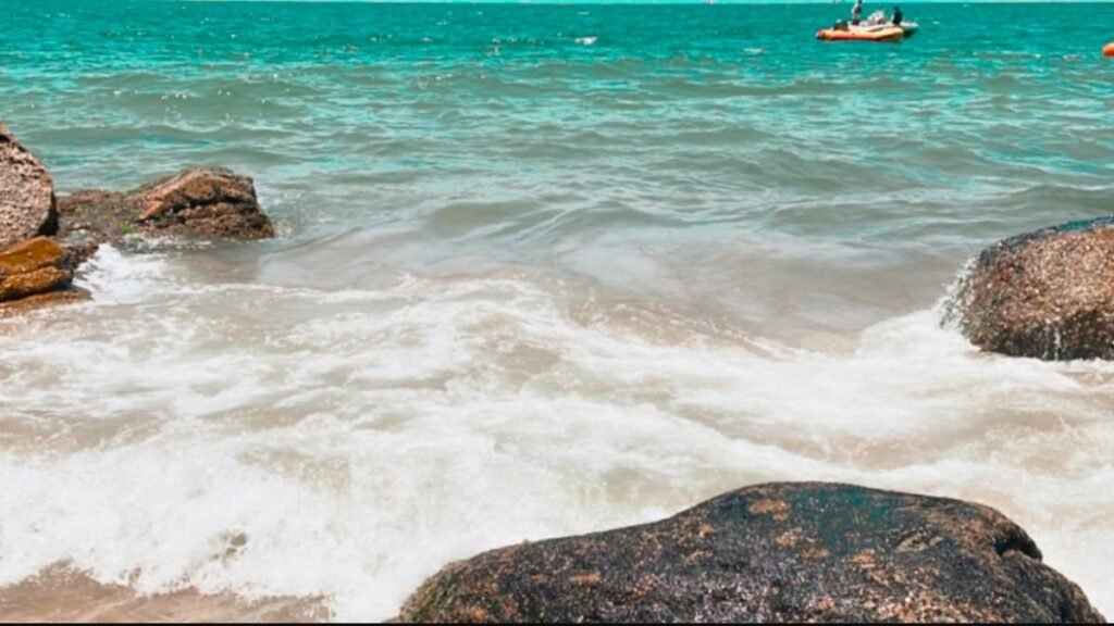Clima em Balneário Camboriú: melhor época para viajar e como é o tempo em cada estação 4 Ondas chegando à areia entre rochas em uma praia de Balneário Camboriú, com água azul e céu parcialmente ensolarado.