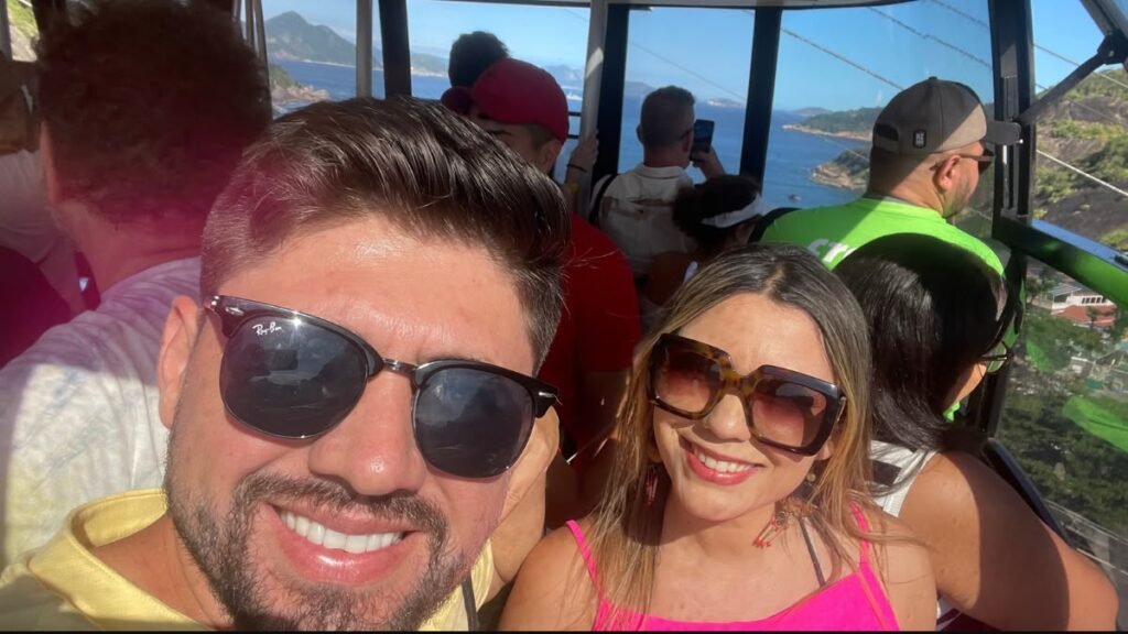 Casal sorrindo dentro do bondinho do Pão de Açúcar, junto a outros visitantes durante o passeio no Rio de Janeiro.