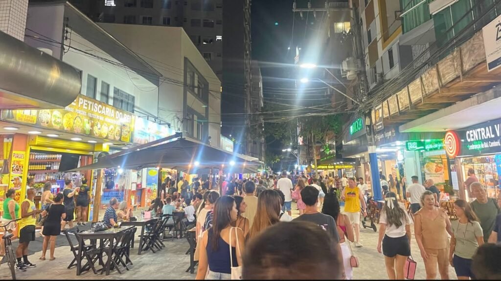 Calçadão de Balneário Camboriú à noite com restaurantes, mesas e grande circulação de pessoas.