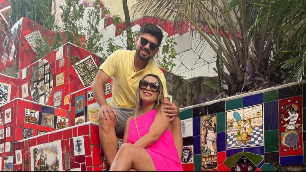 Casal posando na Escadaria Selarón, cercado por degraus decorados com azulejos coloridos.