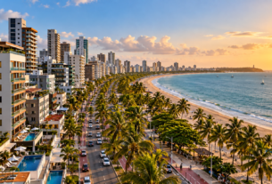 Vista aérea da orla de João Pessoa com hotéis, prédios residenciais, coqueiros, avenida e praia.