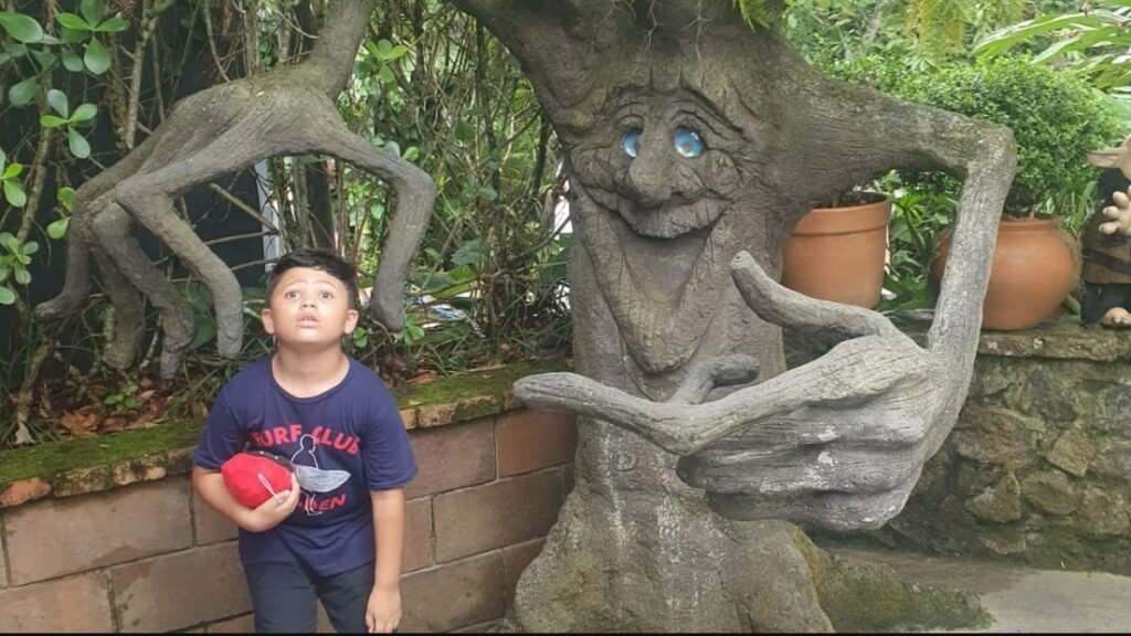Lucas ao lado de uma escultura de árvore com rosto na Fantástica Floresta do Parque Unipraias.