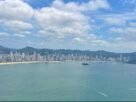 Vista panorâmica da Praia Central de Balneário Camboriú, com o mar, os edifícios altos e as montanhas ao fundo.