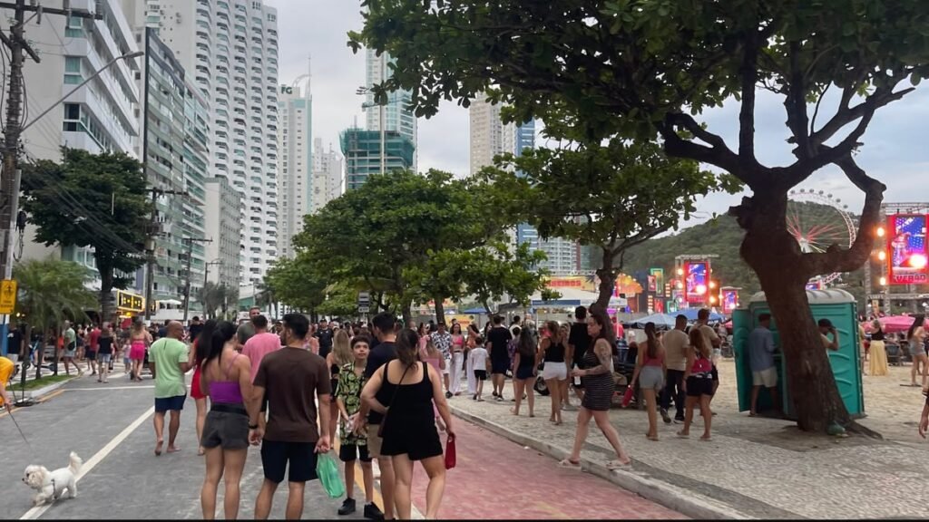 Passeios gratuitos em Balneário Camboriú: orla da Praia Central lotada durante o Carnaval, com foliões, prédios altos e a roda-gigante ao fundo.