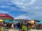 Clima em Balneário Camboriú no verão, com céu parcialmente nublado, guarda-sóis e praia movimentada.
