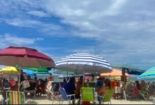 Clima em Balneário Camboriú no verão, com céu parcialmente nublado, guarda-sóis e praia movimentada.