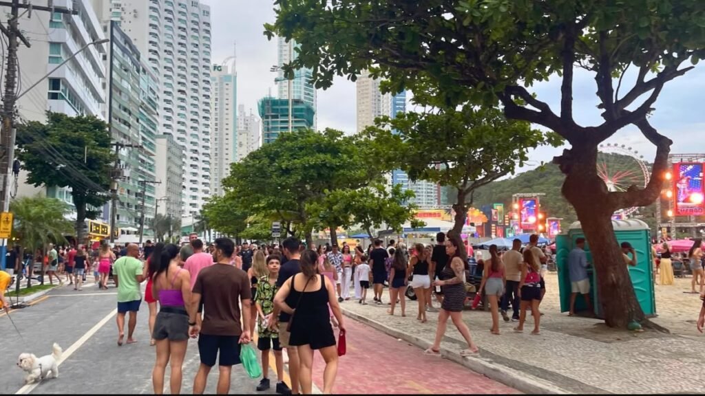 Pessoas caminhando pela orla da Praia Central de Balneário Camboriú durante o Carnaval, com a roda-gigante ao fundo.
