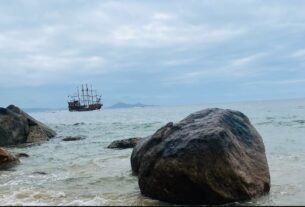Barco turístico ao longe, mar e grandes rochas no litoral de Balneário Camboriú.