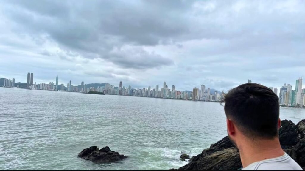 Rafa observando o mar e os prédios de Balneário Camboriú em um dia nublado.