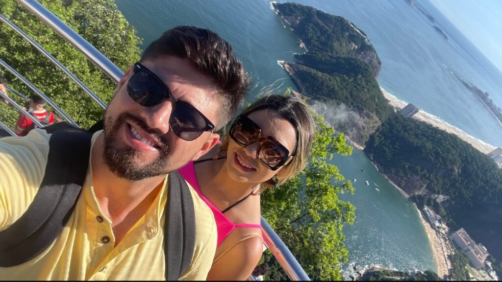 Casal no alto do Pão de Açúcar com vista para o mar e as paisagens do Rio de Janeiro.